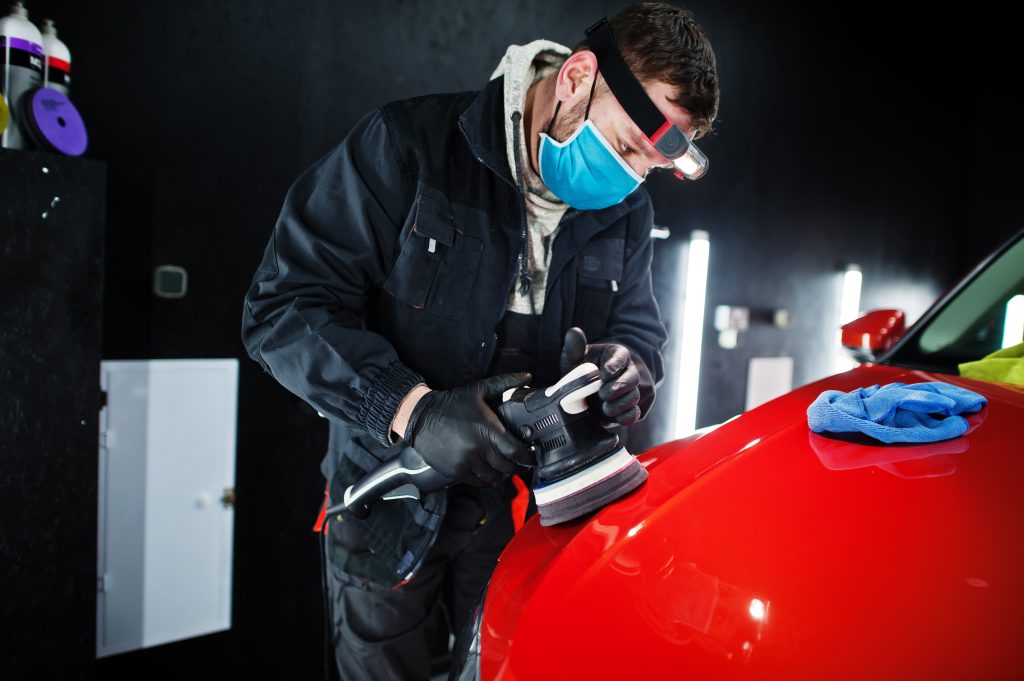 Car detailing concept. Man in face mask with orbital polisher in